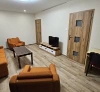 Living room in a two-room apartment with orange furniture and a wooden decor floor.