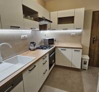 A kitchen in a 2-room apartment with white cabinets and a wooden decor floor.