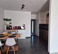 A kitchen in a 3-room apartment with a dining table, dark floor, and white chairs.
