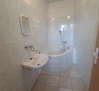 Bathroom in a building with a corner bathtub, white sink, and light tiles.