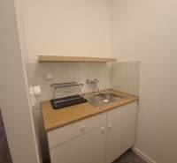 Kitchen corner with sink and drainer, building, light tiles, white cabinet.