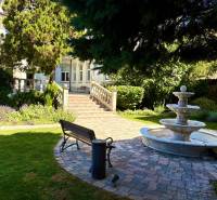 A garden with a fountain, bench, and greenery in front of the building.