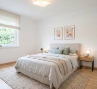 A bright bedroom with a wood-patterned floor, a bed with a light bedspread, and paintings on the wall.
