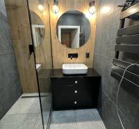 Bathroom in a 2-room apartment with a sink on a black cabinet table and a round mirror.