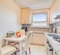 A kitchen in a 4-room apartment with a dining table, cream chairs, and a kitchen unit.