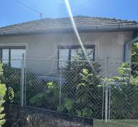 A family house in Tvrdošovce with a fence and greenery, under a clear sunny sky.