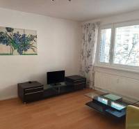 Living room with wood-patterned flooring in a three-room apartment, includes a television and a table.