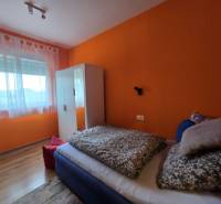 A bedroom in a holiday apartment with a bed, orange walls, and a wood-patterned floor.