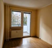 An empty room in a 3-room apartment with a wood-patterned floor and glass doors leading to the balcony.