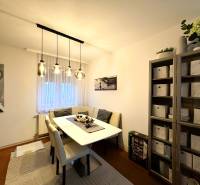A dining room with a table, chairs, and a shelf in a 3-room apartment with decorative lighting.