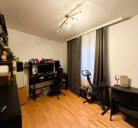 A room with a wood-patterned floor, a desk, a computer, a stationary bike, shelves.