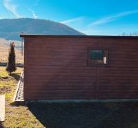 A small wooden house on the street in Prosačov with a view of the hills and blue sky.