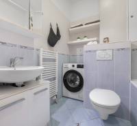 Bathroom in a studio apartment with a washing machine, sink, and bathtub, light blue tiles.