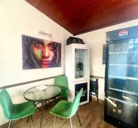 Gastro premises with a wooden decor floor, green chairs, paintings, and a refrigerator.