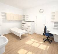 A white office with a sink and wood-patterned flooring, furnished with a desk and cabinets.