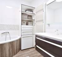 A bathroom with a bathtub, a wooden decor floor, and storage cabinets in a 3-room apartment.