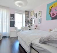 A bedroom in a three-room apartment with a wood-patterned floor and art paintings on the wall.