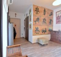 A hallway in a 3-room apartment with armchairs, paintings, and a wooden-patterned floor.