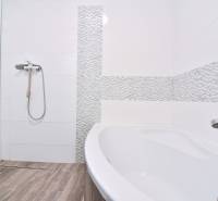 A bathroom with white tiles, a shower, a bathtub, and a wooden decor floor in a 3-room apartment.