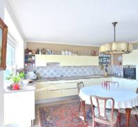 A kitchen in a 3-room apartment with wooden furniture, flowers, and a patterned carpet.