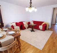 Living room in a 4-room apartment with red sofas, a dining table, and a wooden decor floor.