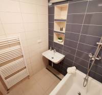 A bathroom in a 4-room apartment with a bathtub, a sink, and storage shelves.