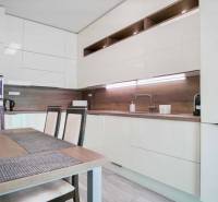 A kitchen in a 3-room apartment with glossy cabinets and wooden wall decor.