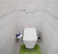 A toilet with white tiles and a green bathroom rug in a 3-room apartment.