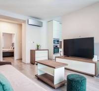 Living room in a three-room apartment with a wooden decor floor, a comfortable sofa, and a television.