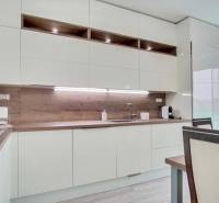 A kitchen in a 3-room apartment with white furniture and a floor with a wooden decor.
