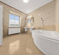 A bathroom in a family house with a bathtub, sinks, a window, and light tiles.