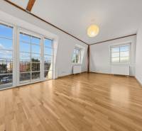 A spacious room with large windows, white walls, and a wooden-patterned floor.