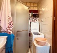 A bathroom in a 3-room apartment with a sink, shower, washing machine, and shelf.