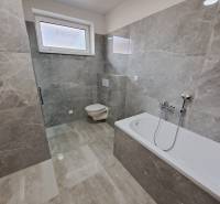 A bathroom with a bathtub and a toilet in a family house, tiled with gray tiles.