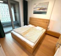 Bedroom in a 2-room apartment with a bed, balcony, and wooden decor flooring.
