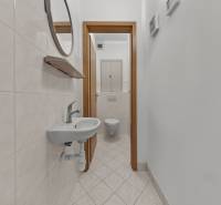 A narrow corridor with an entrance to the toilet, white tiles, a sink, and a mirror in a 4-room apartment.
