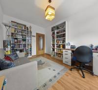 A room in a 4-room apartment with a library, a desk, a sofa, and a floor with a wooden decor.