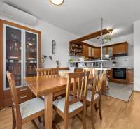 Dining area with wooden furniture and a kitchen in a 4-room apartment with a wood-patterned floor.