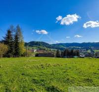 A landscape with a meadow and trees in the Gardens of Ľubietová, surrounded by hills and a blue sky.
