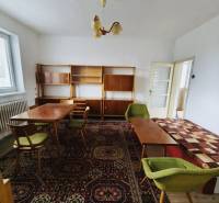 A family house with antique furniture, a carpet with colorful patterns, and green chairs.