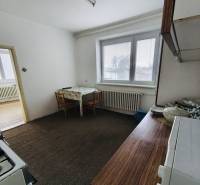 A kitchen with a gas stove and carpet in a family house, white interior, table, window with blinds.
