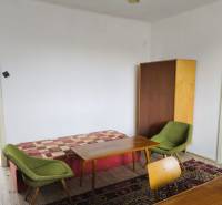 A room of a family house with armchairs, tables, a cabinet, and a wooden-patterned floor.