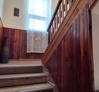 Stairs in a family house with wooden paneling, a railing, and a window with a lace curtain.