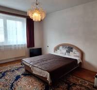 A bedroom in a family house with a bed, a chandelier, and a carpet on a floor with a wooden decor.