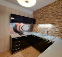 A kitchen in a 2-room apartment with a wooden decor floor and brick cladding on the wall.