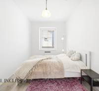 A bright bedroom with a light bed, a pink carpet, and a wood-patterned floor.