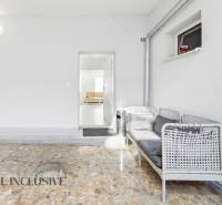 A white room with wicker seating next to a gray door leading to a 3-room apartment.