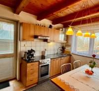 A kitchen in a family house with a wooden ceiling, a floor with a wooden decor, and large windows.