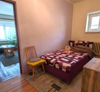 A bedroom in a family house with a bed, a chair, and a wooden decor floor.