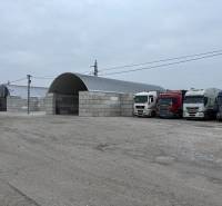 Warehouses and halls in Ladce with parked trucks on a gravel parking lot.